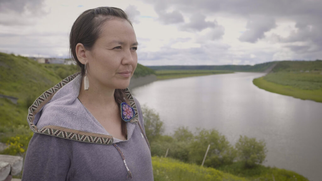 A woman stands on a grassy hill overlooking a wide, winding river under a cloudy sky.